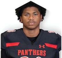 A person with short curly hair wearing a black sports jersey with red accents and the word Panthers on the front is looking directly at the camera. Description generated by AI