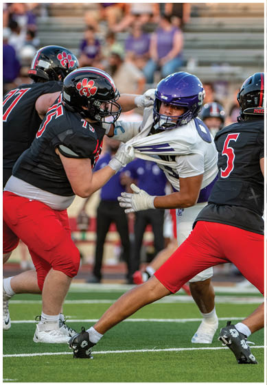 Three people in football uniforms are engaged in a play on a field, with one person in a white jersey being grabbed by the collar by a person in a black jersey and red pants. Description generated by AI