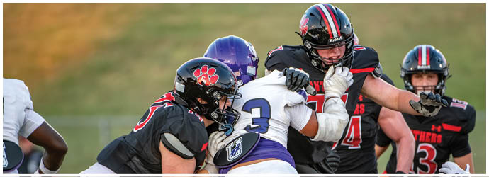People wearing football uniforms are engaged in a close physical play on a grassy field. Description generated by AI
