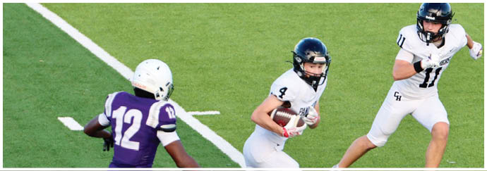 Three people in football uniforms are on a green field with one person in white holding a football while another in purple approaches. Description generated by AI