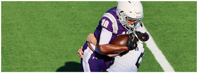 Two people in football uniforms are engaged in a tackle on a green field near a white line. Description generated by AI