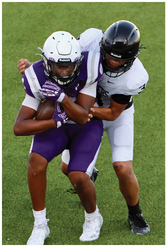 Two people wearing football helmets and uniforms are engaged in a close physical play on a grassy field. Description generated by AI