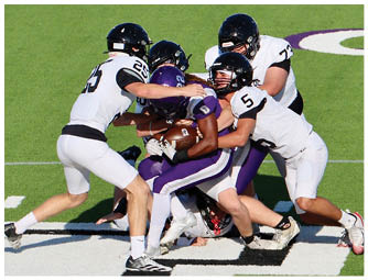 Several people in football uniforms are engaged in a tackle on a grassy field with one person holding the ball tightly. Description generated by AI