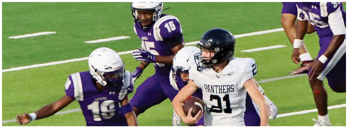 A person wearing a white football uniform with the number 21 is running with the ball while several people in purple football uniforms attempt to catch them on a grassy field. Description generated by AI