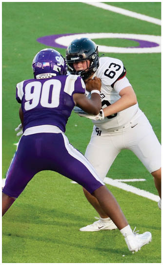 Two people in football uniforms are engaged in blocking on a green field with white yard lines. Description generated by AI