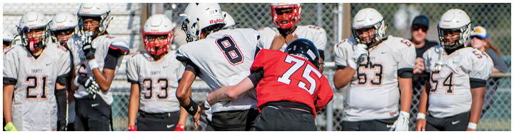 A group of people wearing sports uniforms stand on a field with one person in a red jersey and black pants interacting with others in white jerseys and black pants. Description generated by AI