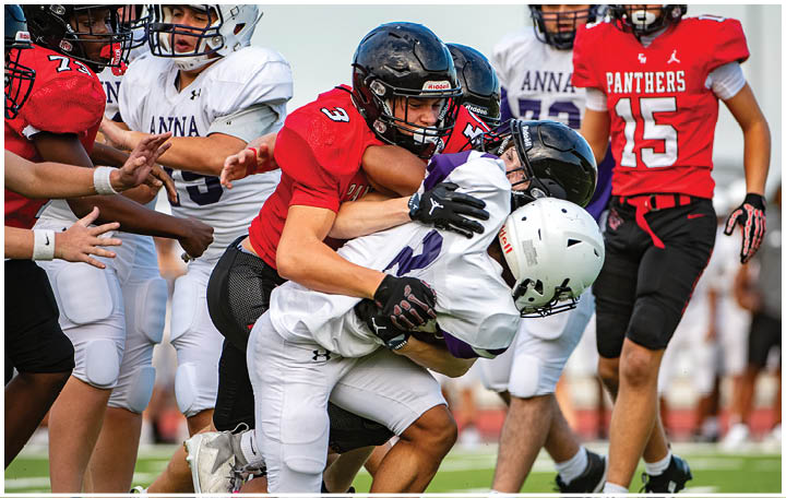 Adults wearing football uniforms are engaged in a tackle during a game on a grassy field. Description generated by AI