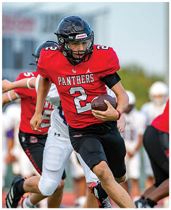 A person wearing a red Panthers football jersey with the number 2 is running with a football while being pursued by other players on a field. Description generated by AI