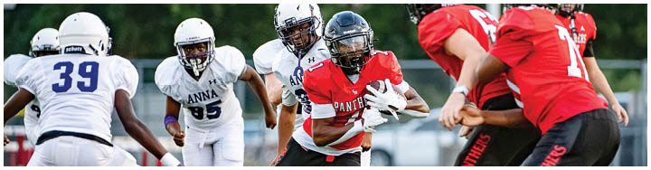 People wearing football uniforms are actively engaged in a game on a field, with one person holding the ball and others preparing to block or tackle. Description generated by AI