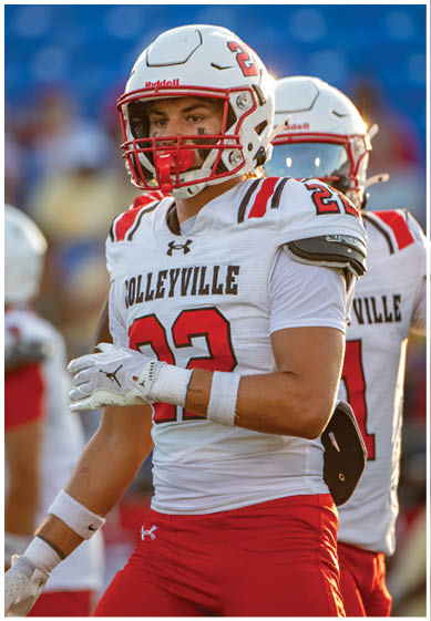 A person wearing a white and red football uniform with the number 22 and a helmet stands on a field with another similarly dressed person in the background. Description generated by AI