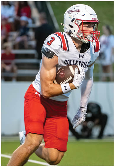 A person wearing a white football helmet and red and white uniform is running on a football field while holding a football. Description generated by AI