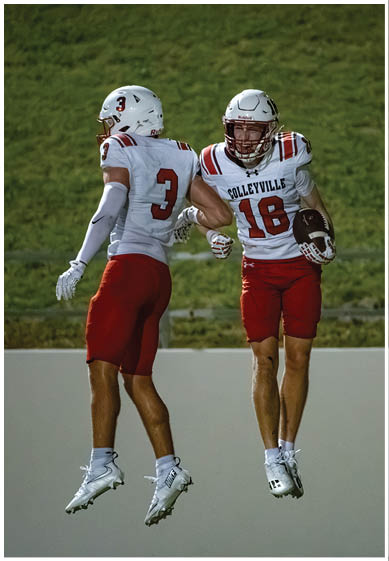Two people in football uniforms with helmets are bumping elbows on a grassy field. Description generated by AI