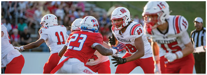 People wearing red and white sports uniforms are actively engaged in a football game on a grassy field. Description generated by AI
