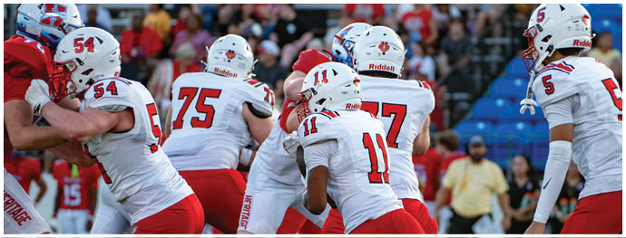 A group of people wearing white and red football uniforms are gathered on a field with a crowd in the background. Description generated by AI