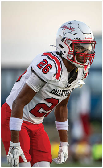 A person wearing a white and red football uniform with the number 26 is in a ready stance on a field. Description generated by AI