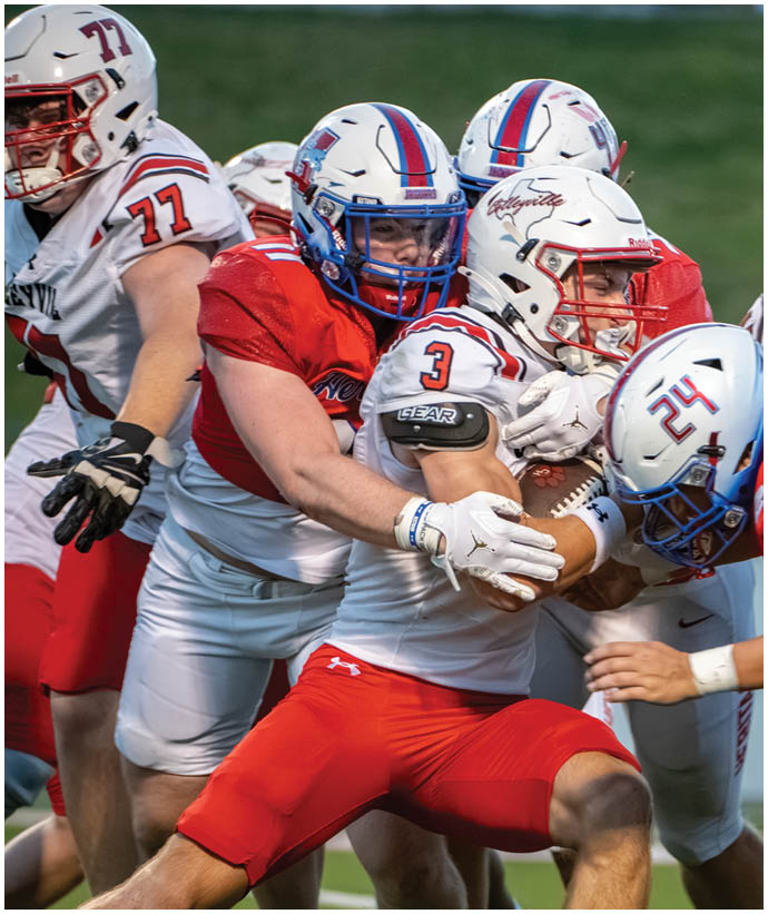 People in football uniforms are engaged in a tackle during a game on a grassy field. Description generated by AI