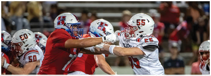 Two people in football uniforms are engaged in a physical struggle on the field during a game. Description generated by AI