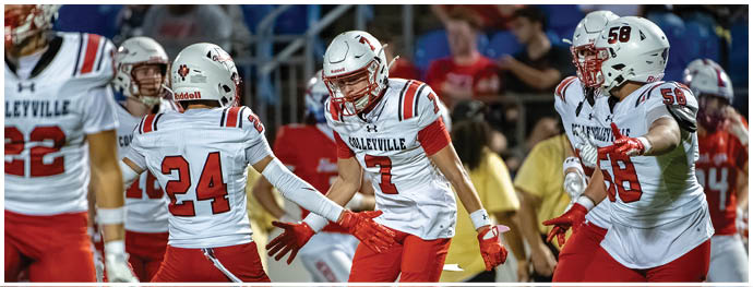 Four people in white and red football uniforms are celebrating on a field during a game. Description generated by AI