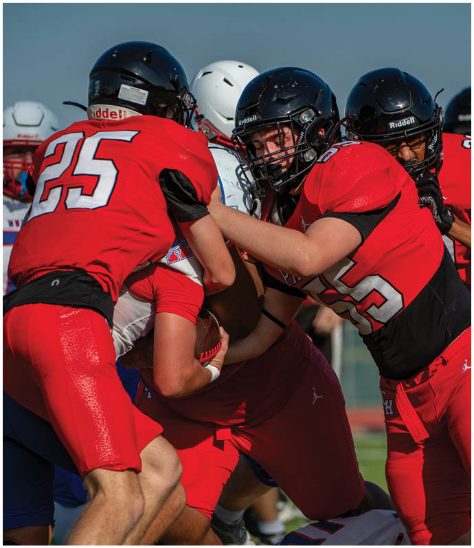Several people wearing football helmets and uniforms are engaged in a close physical play on a football field. Description generated by AI