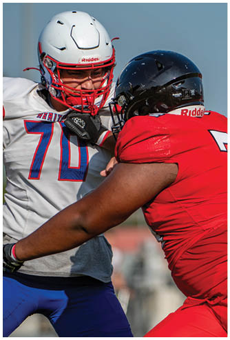 Two people wearing football helmets and uniforms are engaged in a physical play on a football field. Description generated by AI