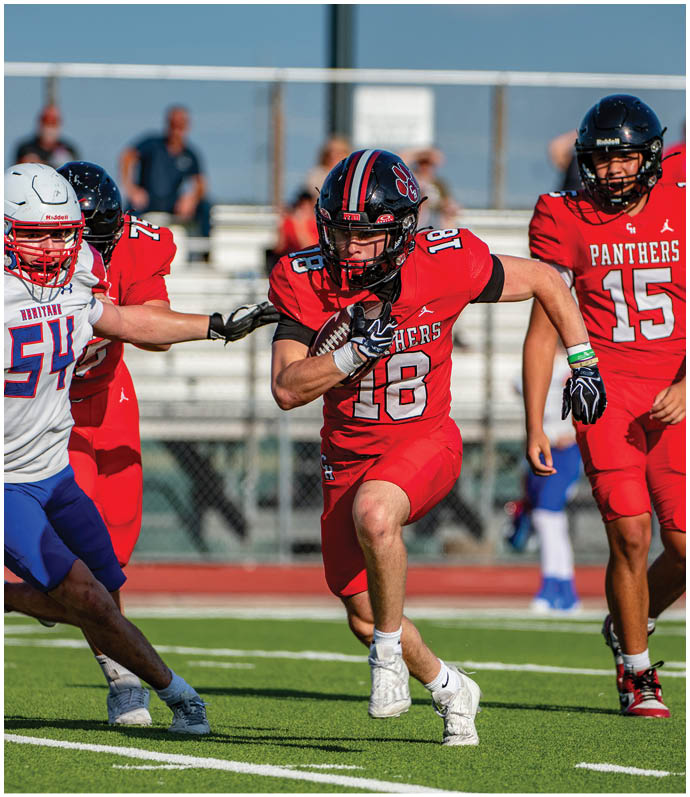 A person in a red football uniform with the number 18 is running with the ball while being pursued by a person in a white and blue uniform and accompanied by two other players in red uniforms on a football field. Description generated by AI