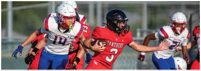 A person in a red football uniform with the number 3 is running with the ball while being pursued by people in white and blue uniforms on a football field. Description generated by AI