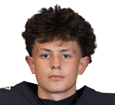 Person with short curly hair wearing a dark sports jersey looking directly at the camera against a white background. Description generated by AI