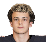 Person with curly hair wearing a dark sports jersey looking directly at the camera against a white background. Description generated by AI