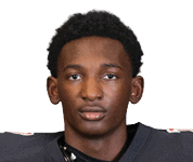 A person with short curly hair wearing a dark sports jersey looks directly at the camera against a white background. Description generated by AI