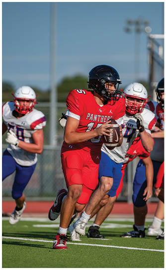A person wearing a red football uniform and black helmet is holding a football and appears to be preparing to throw it during a game. Description generated by AI