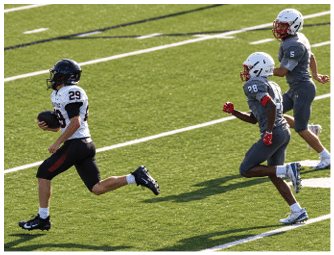 A person wearing a white and black football uniform is running with the ball while two people in gray football uniforms chase behind on a green field. Description generated by AI