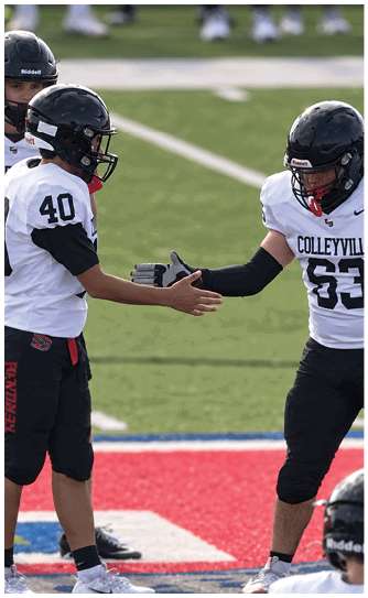 Three people in football uniforms and helmets are on a field, with two of them reaching out to shake hands. Description generated by AI