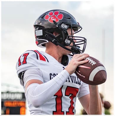 A person wearing a black football helmet and white jersey with the number 17 is preparing to throw a football. Description generated by AI