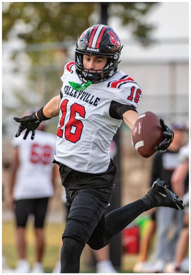 A person wearing a football helmet and a white jersey with the number 16 is reaching out to catch or hold a football. Description generated by AI