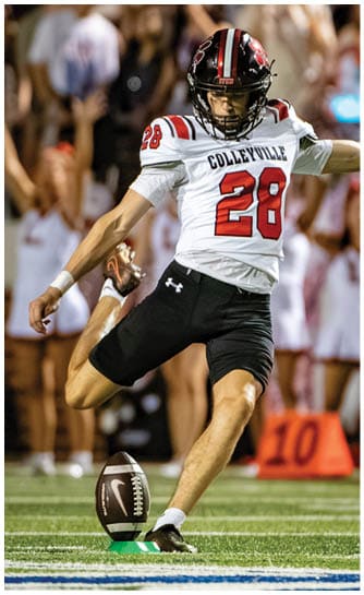 A person wearing a football uniform with the number 28 is kicking a football on a field with a crowd of people and cheerleaders in the background. Description generated by AI