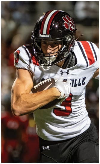 A person wearing a football uniform and helmet is running while holding a football tightly. Description generated by AI