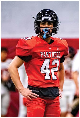 A person wearing a red football uniform with the number 42 and the word Panthers stands with hands on hips on a sports field. Description generated by AI
