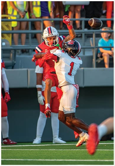 Two people in football uniforms are competing to catch a football in mid-air during a game. Description generated by AI