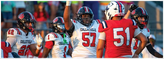 Five football players in helmets and uniforms are interacting on the field, with one player raising an arm in celebration. Description generated by AI