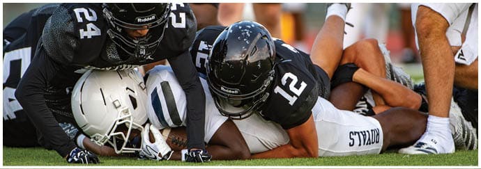 Two people in black football uniforms are tackling a person in a white football uniform during a game. Description generated by AI