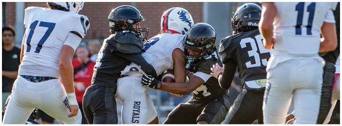 People wearing football uniforms are engaged in a close physical play on a grassy field. Description generated by AI