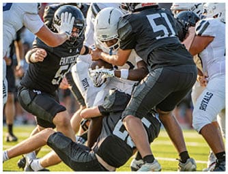 Several football players in black and white uniforms are engaged in a tackle on a grassy field during a game. Description generated by AI
