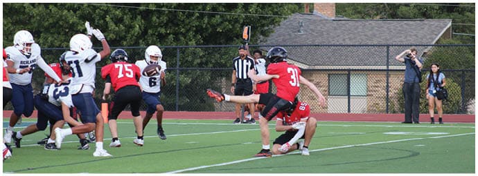 People in football uniforms are actively playing on a field with a referee observing nearby. Description generated by AI