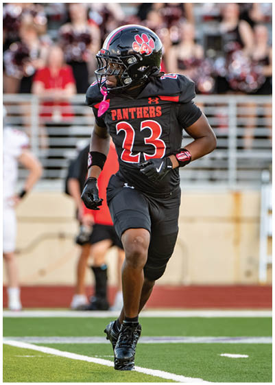 A person wearing a black football uniform with the number 23 and the word Panthers is running on a football field. Description generated by AI