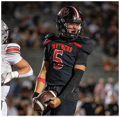 A person wearing a black football uniform with the number 5 and the word Panthers is holding a football while another person in a white uniform is partially visible nearby. Description generated by AI