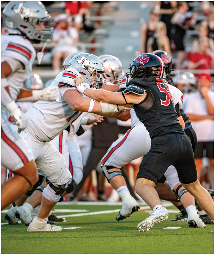 Several people in football uniforms and helmets are engaged in a play on the field, with one player pushing against an opponent. Description generated by AI