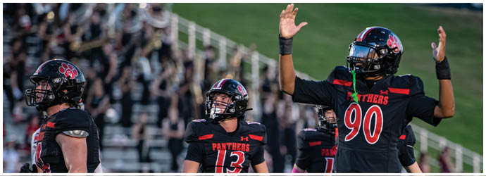 People in black and red football uniforms are on a field with one raising both hands, and a crowd is visible in the background. Description generated by AI