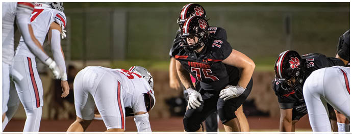Several people in football uniforms are positioned on a field preparing for a play during a game. Description generated by AI