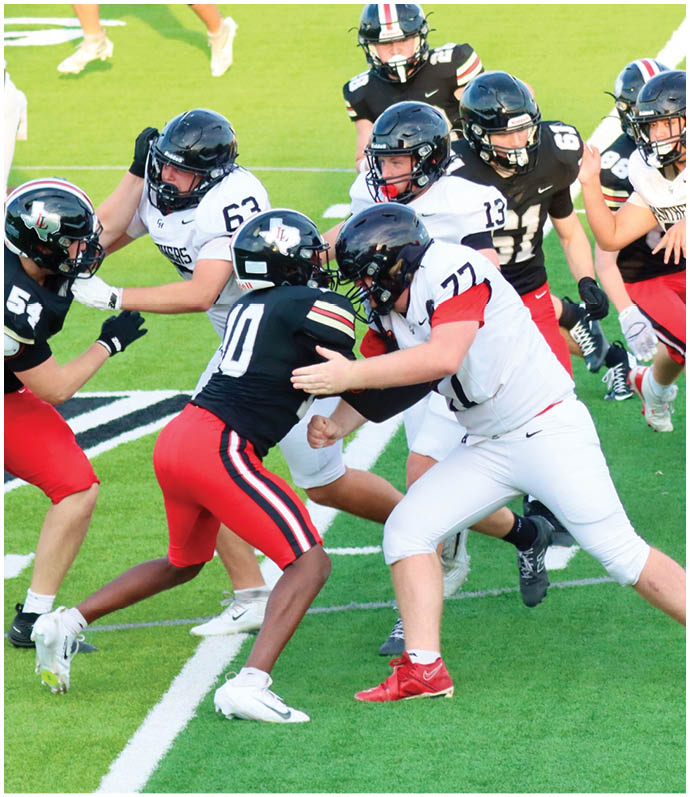 Several people wearing football helmets and uniforms are engaged in a play on a green field with white markings. Description generated by AI