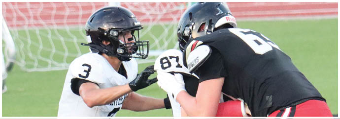 Two people wearing helmets and sports gear are engaged in a football game on a field with a goalpost and track in the background. Description generated by AI